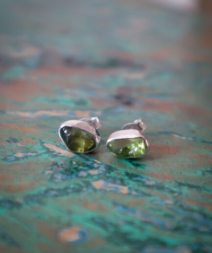 Een paar zilveren oorknoppen met ruwe, groene peridot stenen